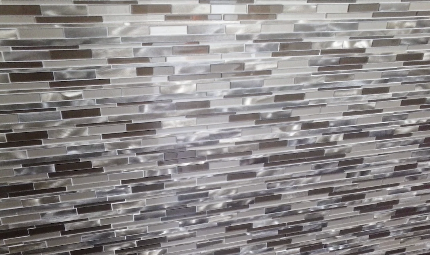 Gray and brown linear mosaic tile backsplash with varied glass finish